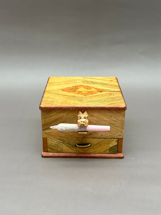 Wooden inlaid rectangular cigarette dispenser box with a cigarette partially ejected from the side mechanism, gray background.