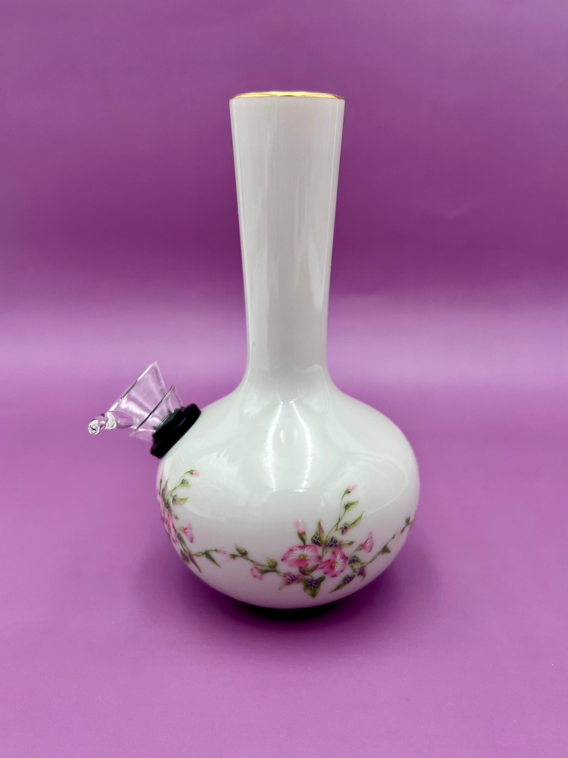Same white bud vase water pipe with pink floral design and gold rim trim, glass bowl piece attached at the side, purple background.