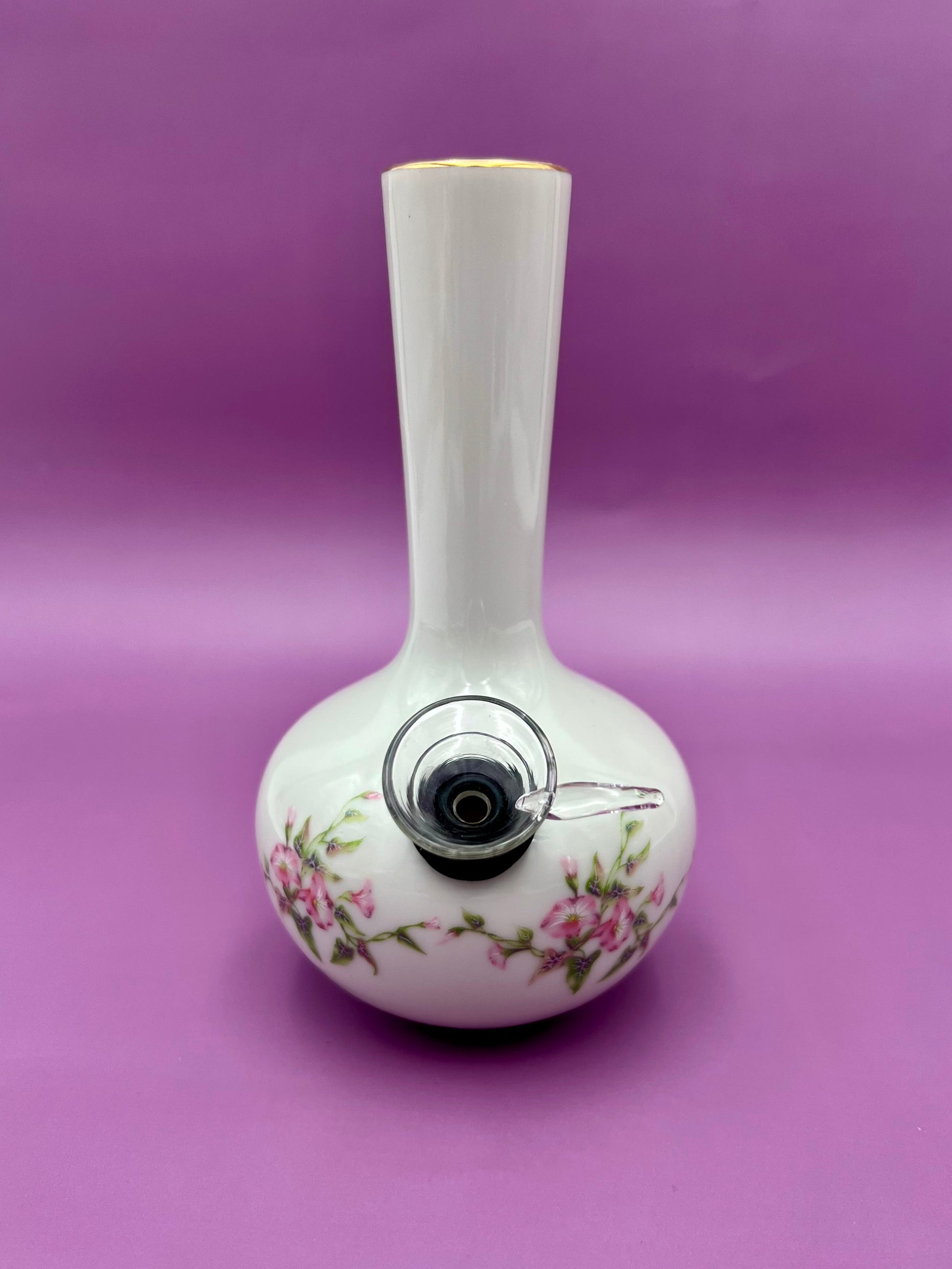 White bud vase water pipe with pink floral design and gold rim trim on a purple background