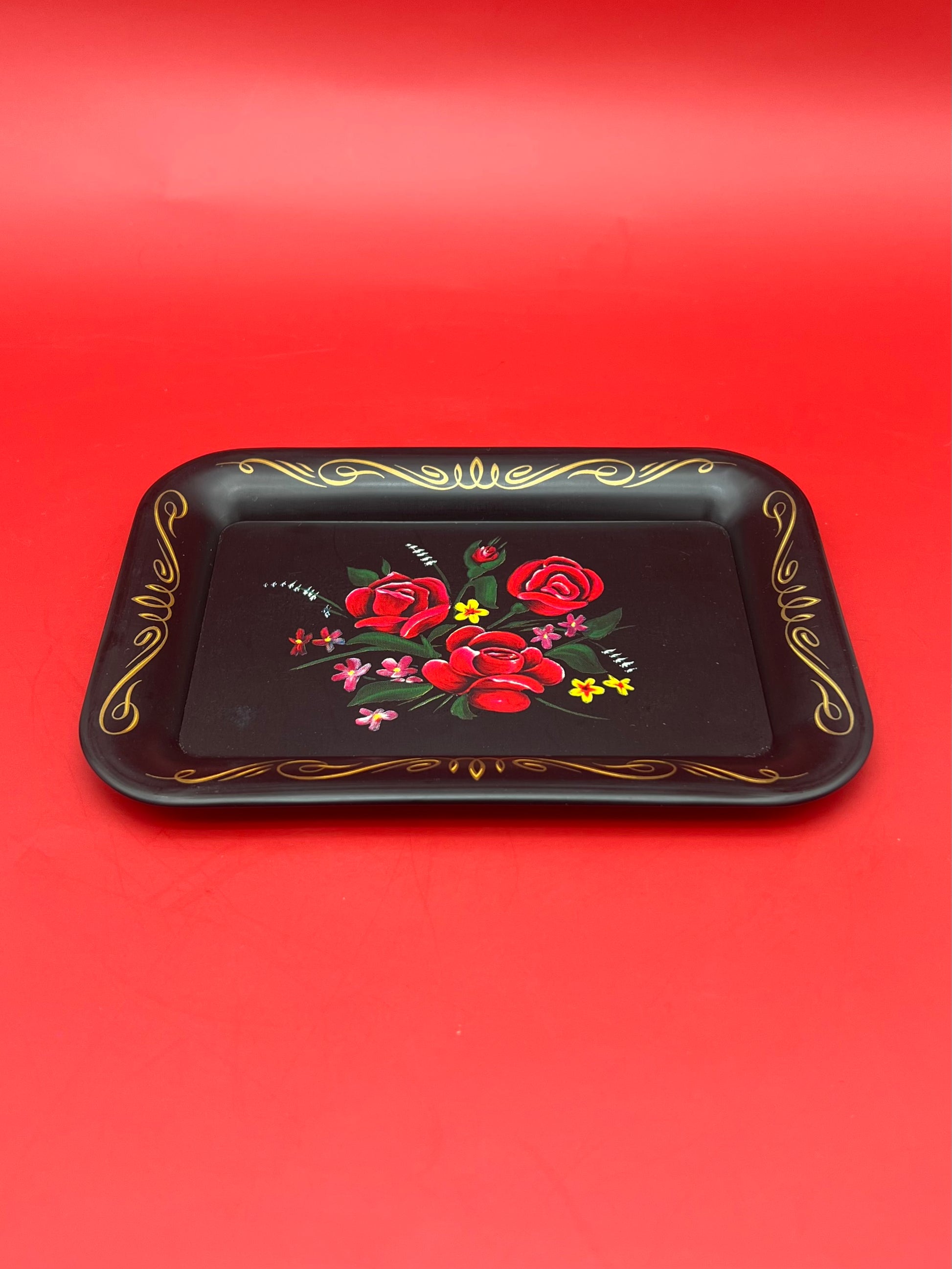 Same black rectangular rolling tray with the red rose design and gold trim, shown as a closer top-down view, red background.