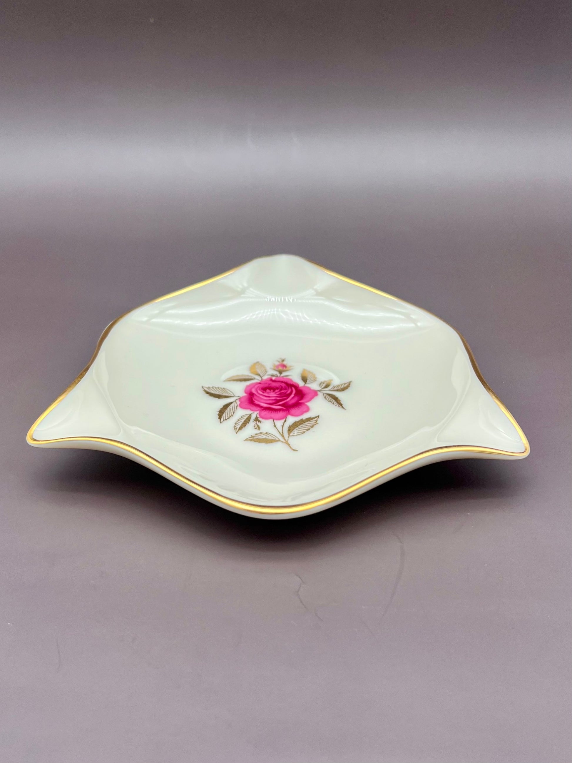 Same star-shaped cream ashtray with its hand-painted pink rose and gold trim, shown without the cigarette pick, gray-mauve background.