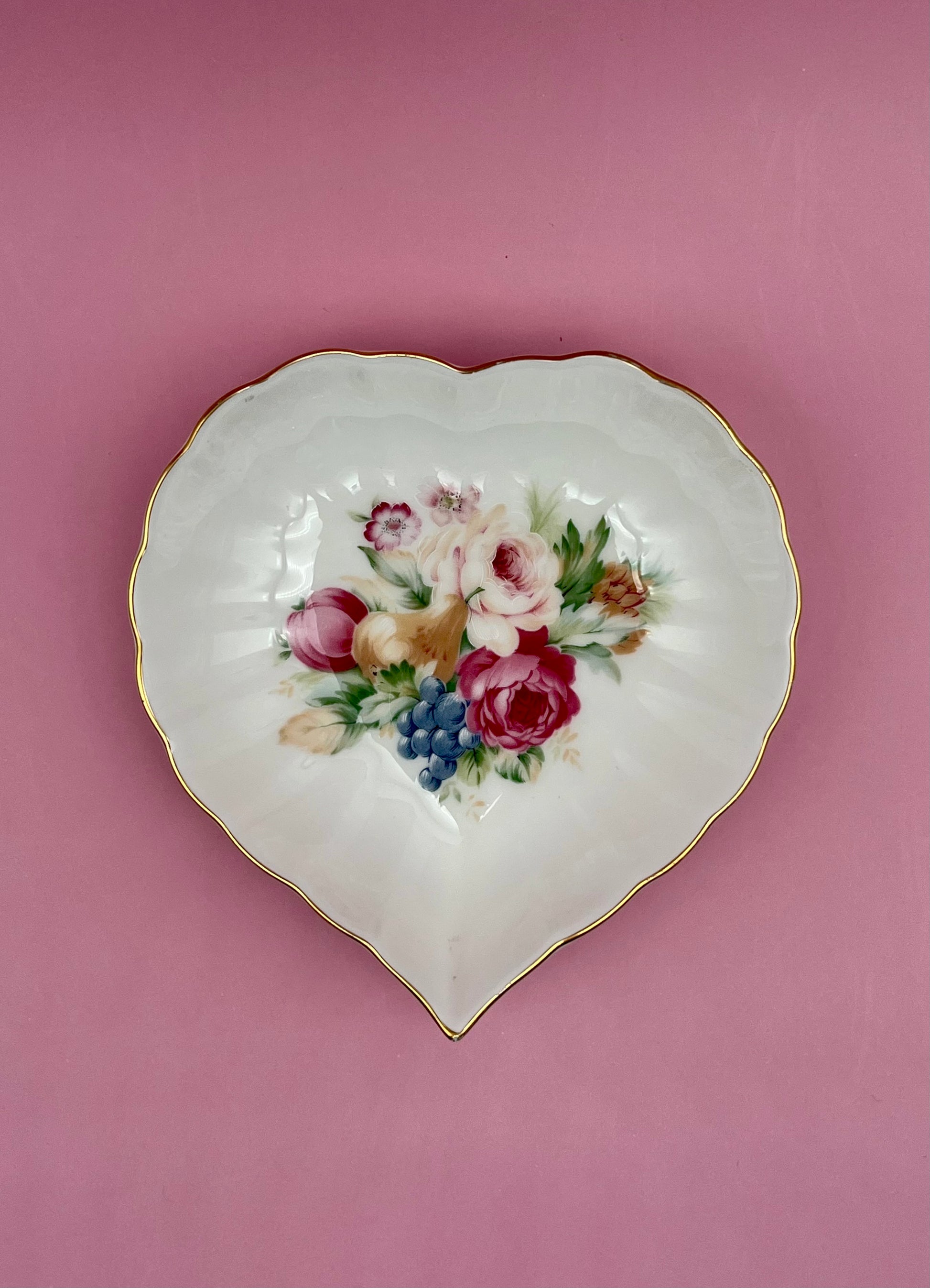 Heart-shaped white porcelain dish with a hand-painted floral bouquet and gold trim, mauve background.