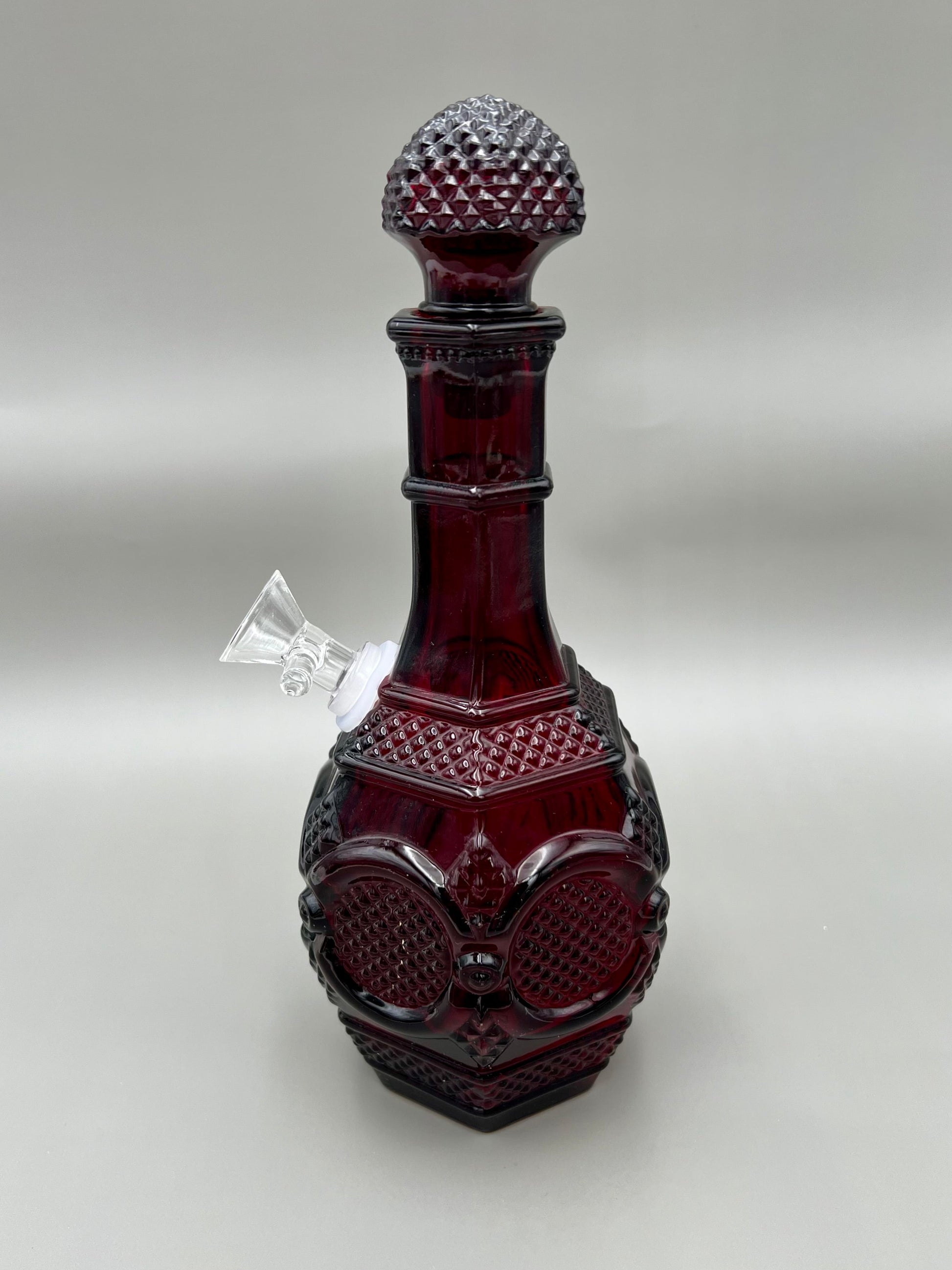 Same ruby red diamond-cut decanter water pipe with its round faceted stopper in place, gray background