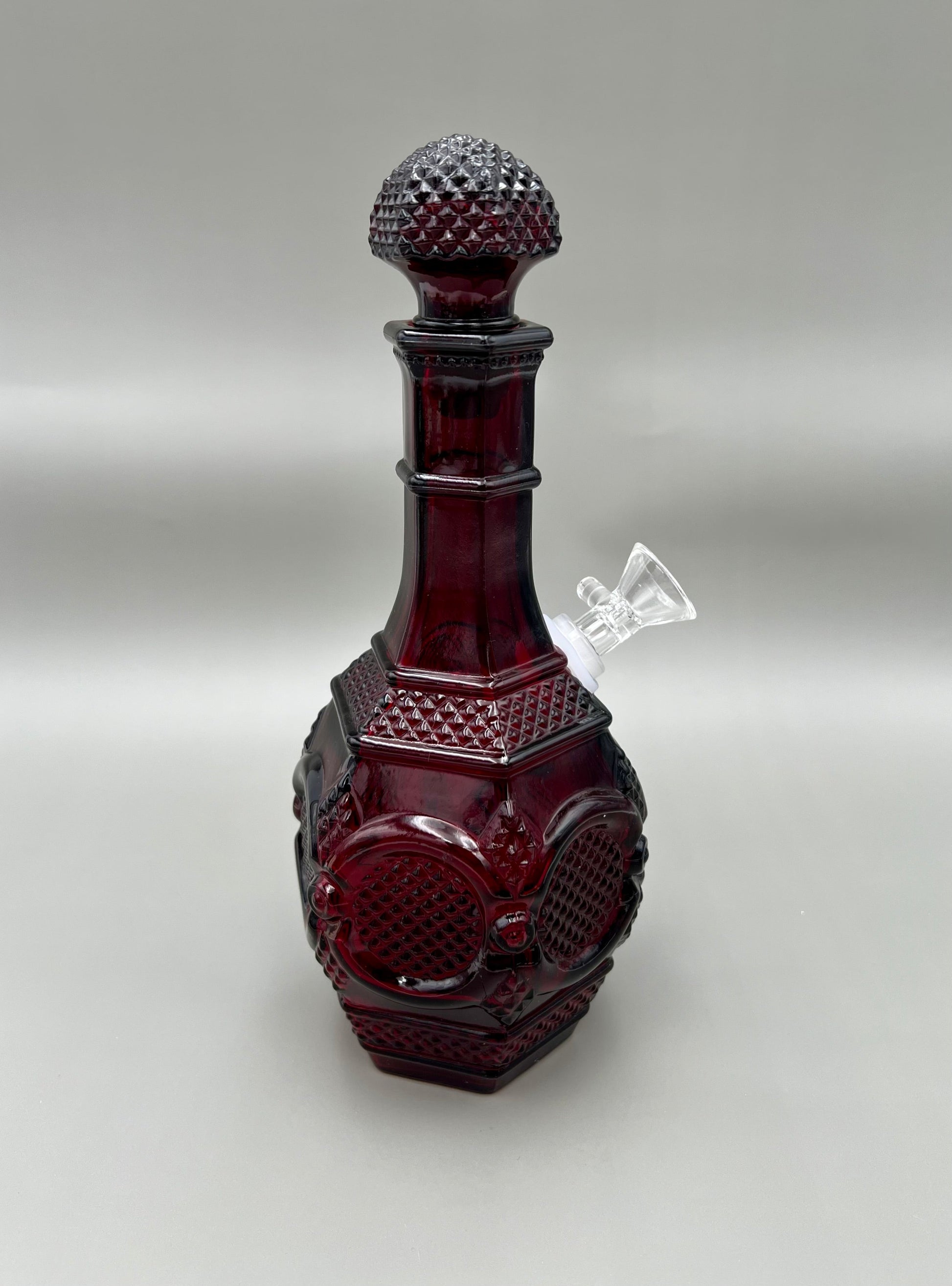 Same ruby red diamond-cut decanter water pipe in a close side view highlighting the hobnail-textured stopper and panel cuts, gray background