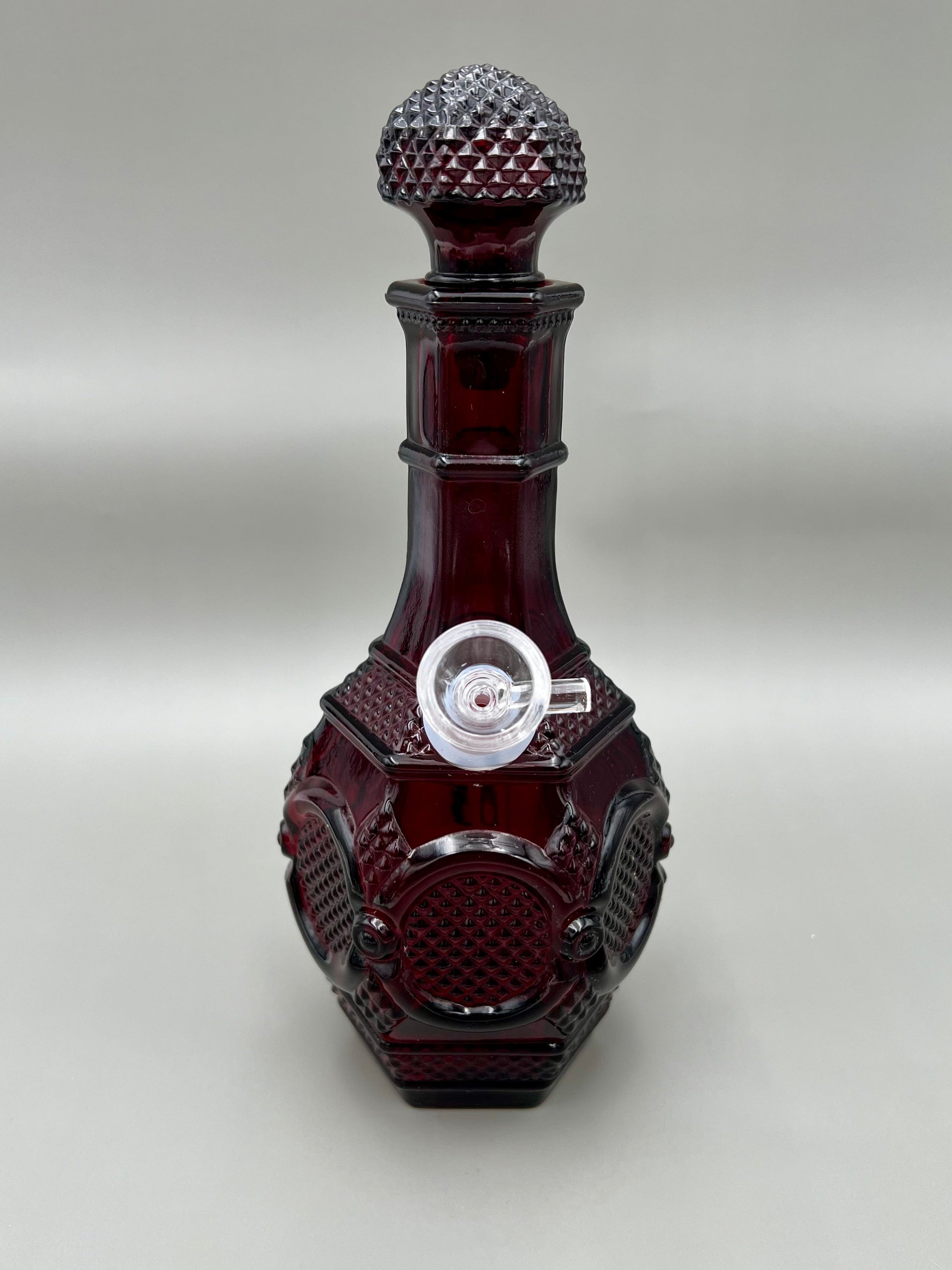 Front view of a deep ruby red glass decanter water pipe with a faceted geometric pattern and matching glass stopper, gray background.