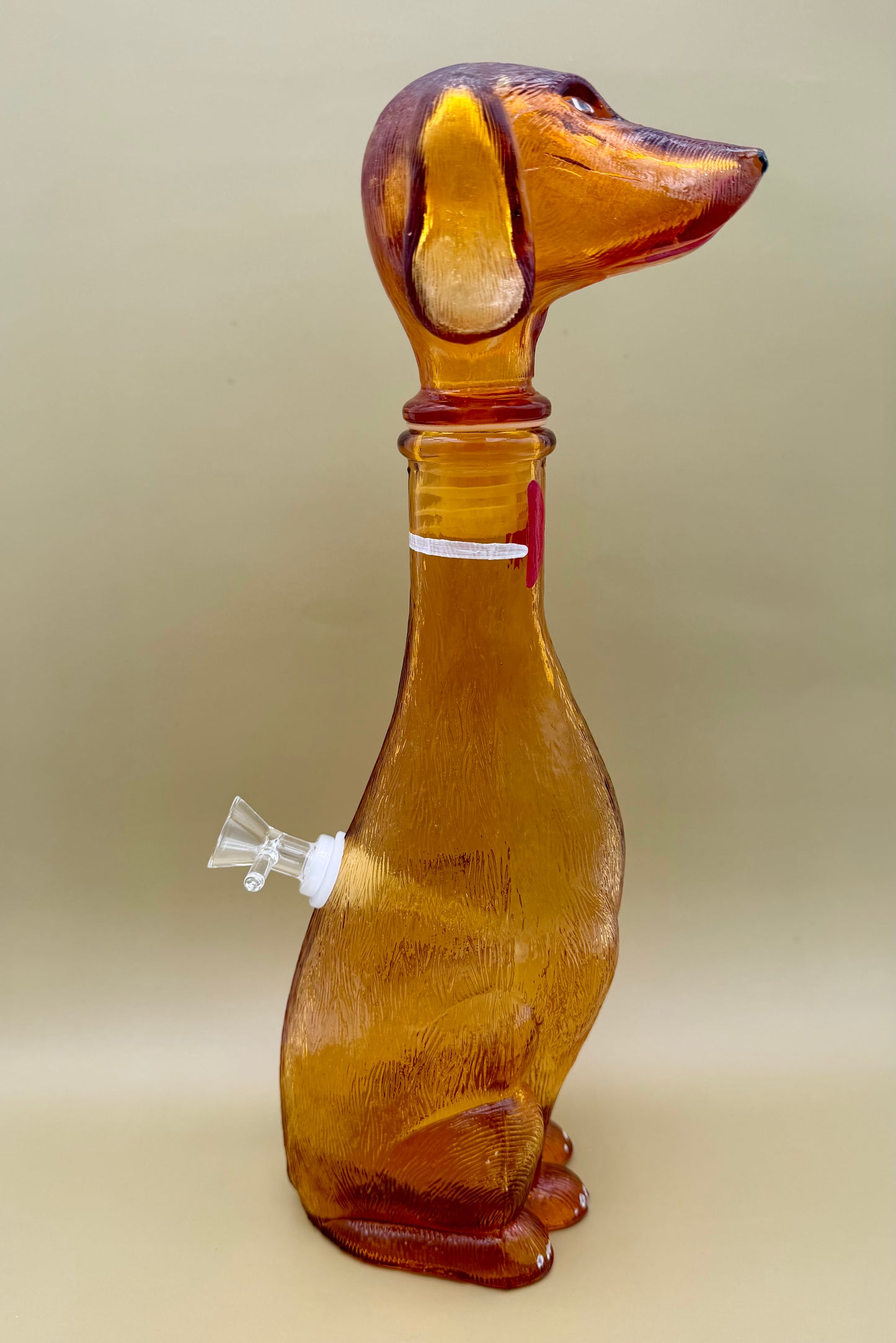 Opposite side profile of the amber glass dachshund decanter showing the glass bowl piece attached, tan background.