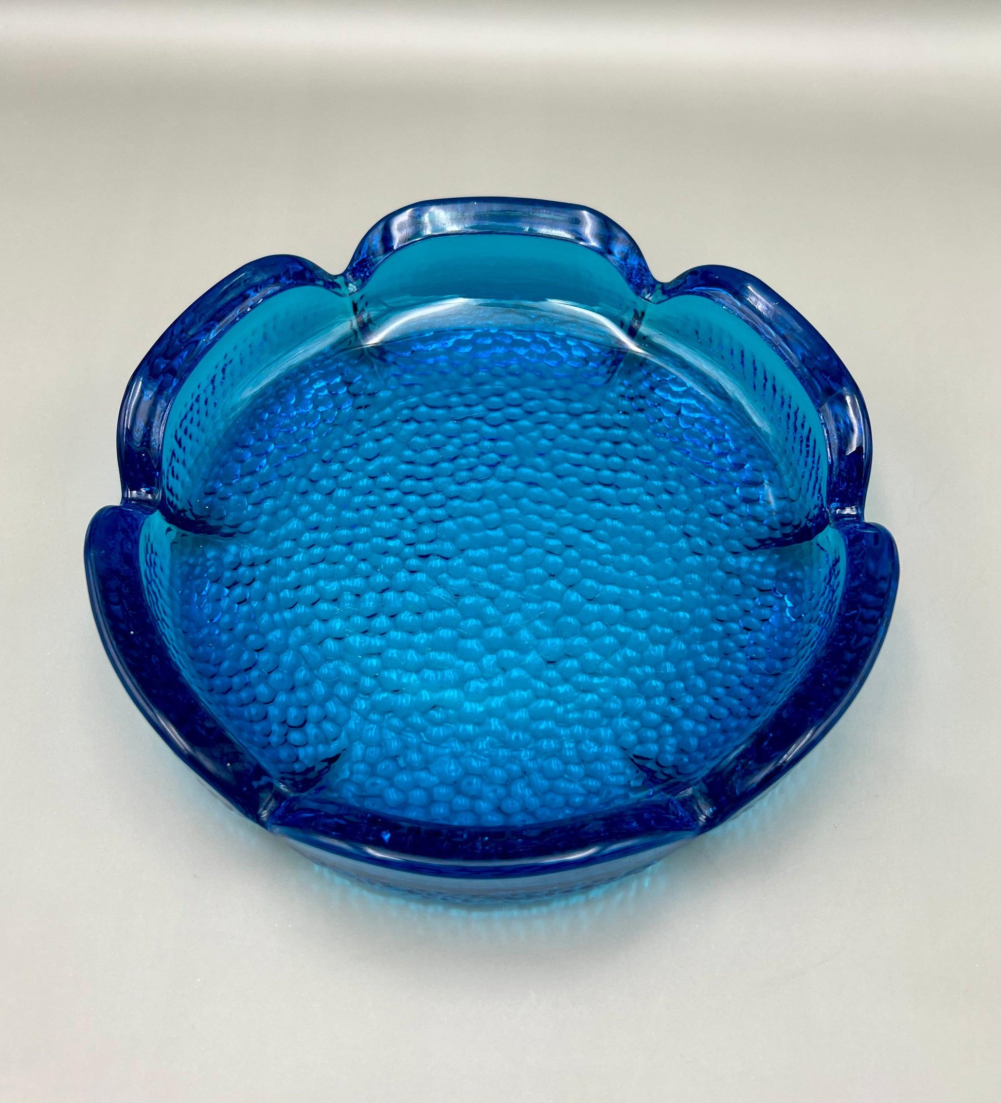Scalloped turquoise glass ashtray shaped like a flower, with a textured bubbled surface, shown without the cigarette pick, gray background.