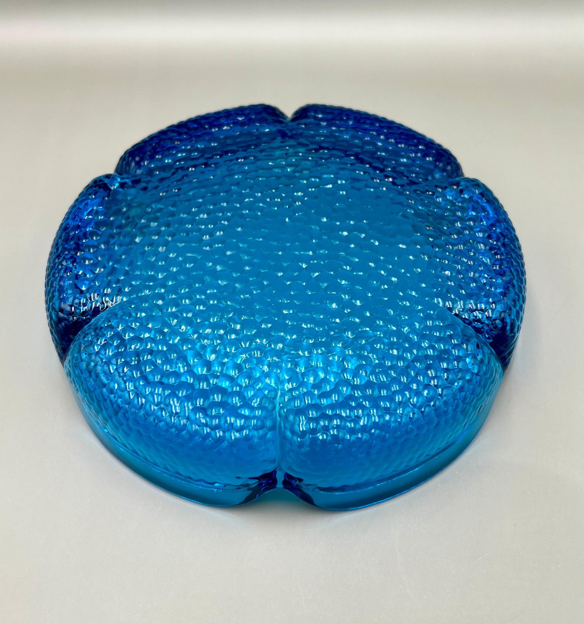 Same scalloped turquoise glass flower-shaped ashtray shown from a top-down angle, gray background.