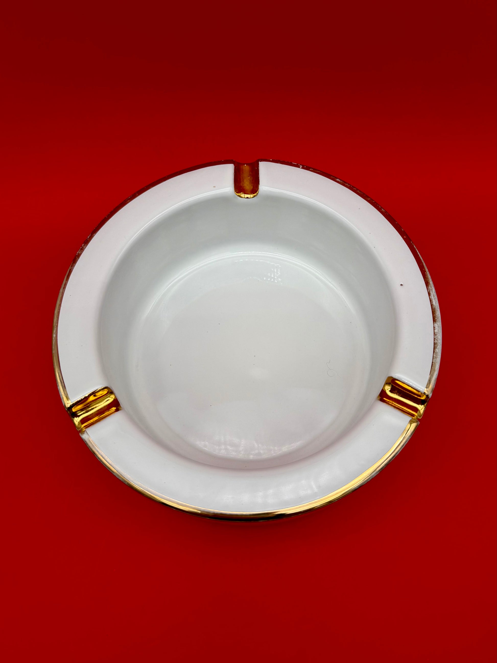 Interior view of the same oval pink and white ashtray showing its gold-trimmed rests, empty bowl, red background.