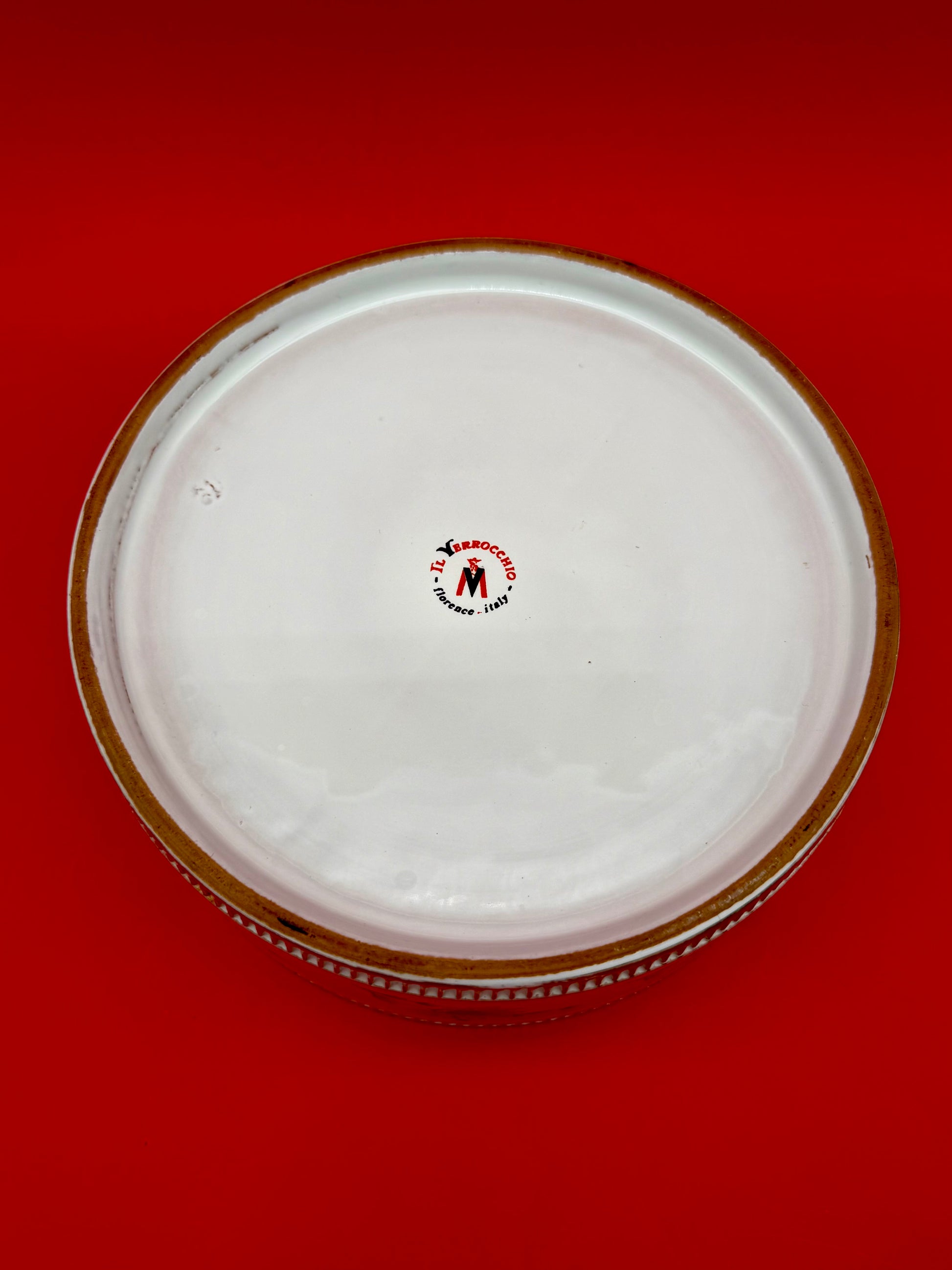 Underside of the same oval ashtray showing a red maker's stamp, red background.