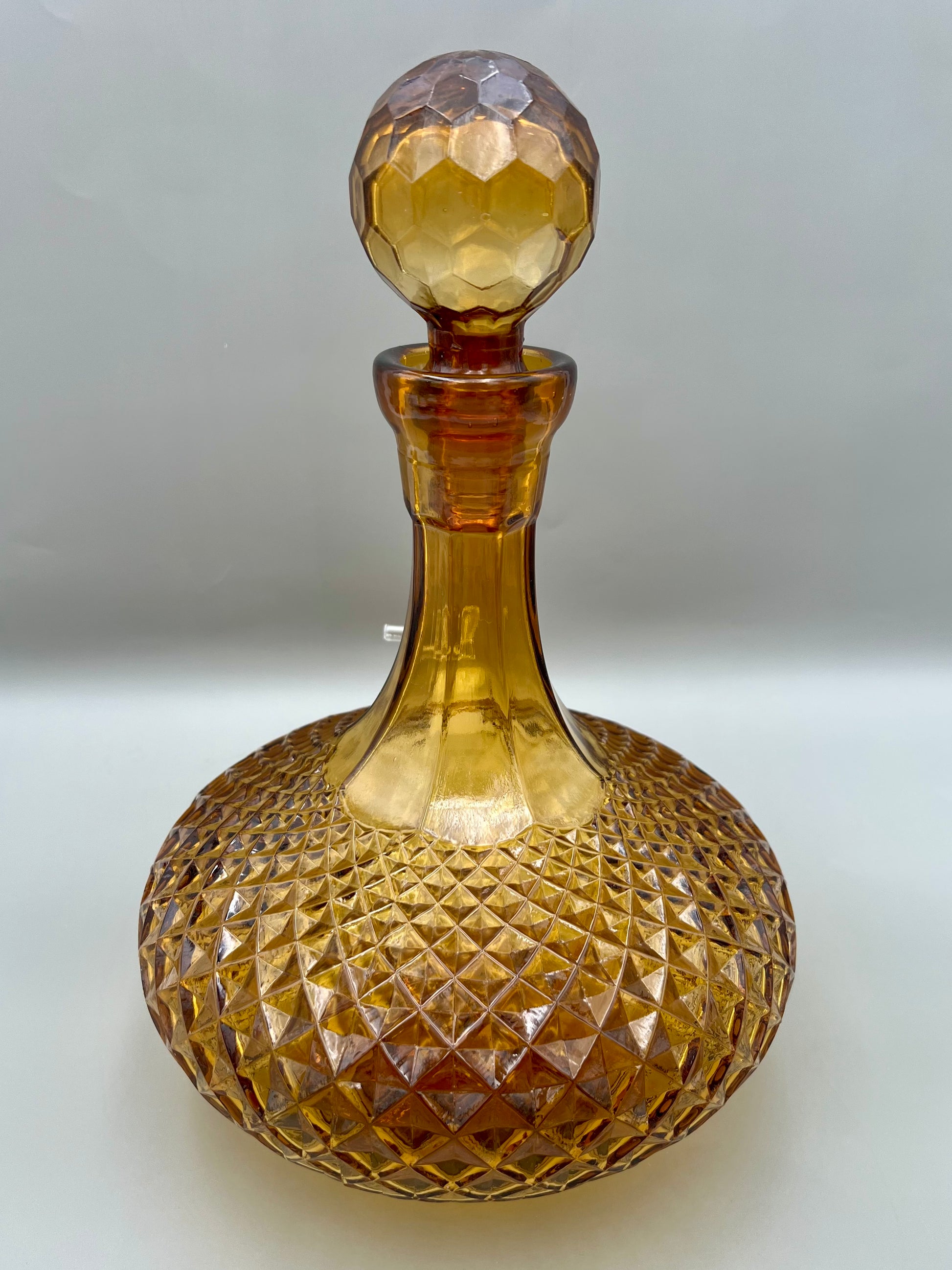 Same amber cut-glass decanter with its stopper in place, shown from a different angle, gray background.