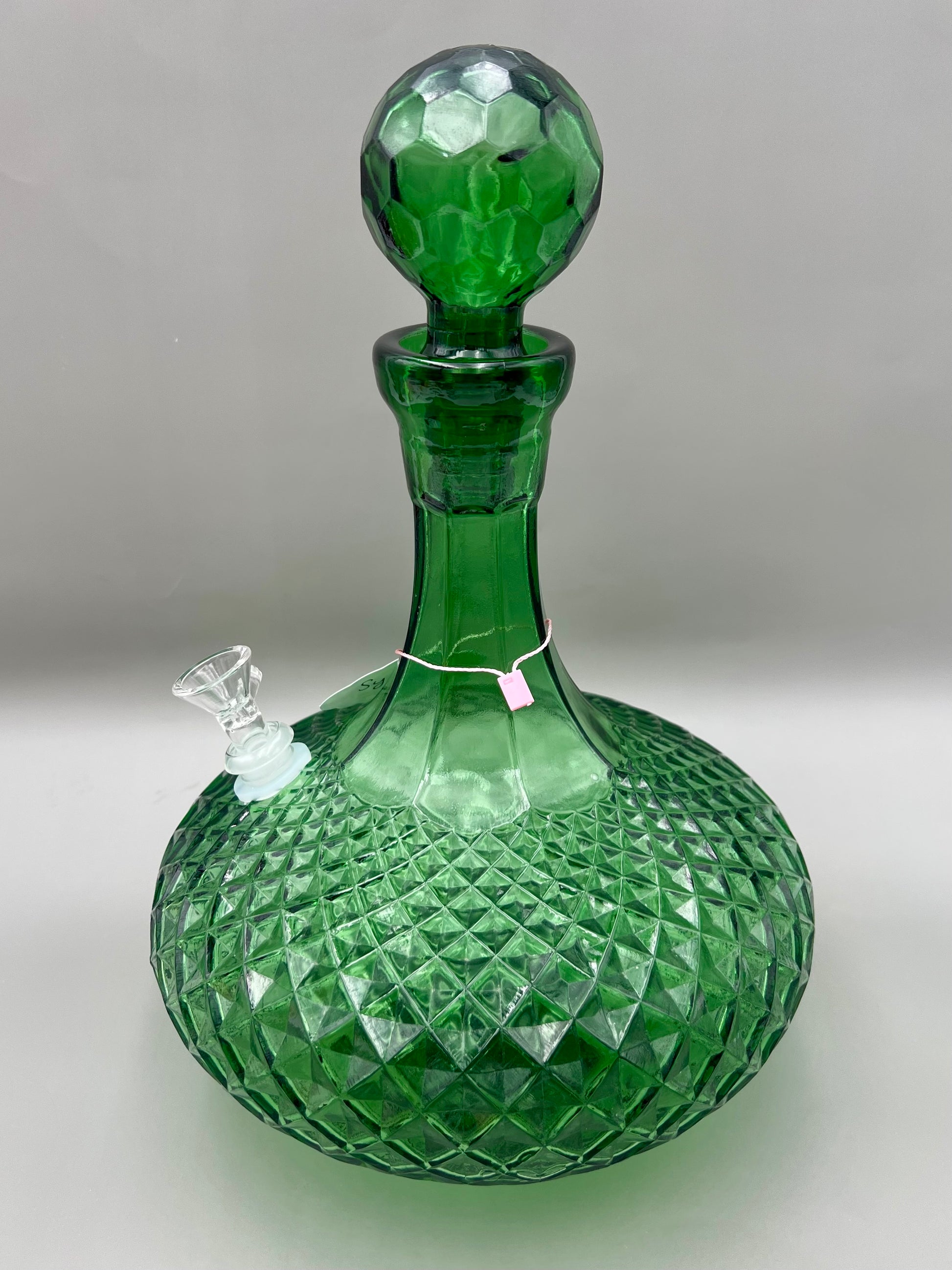 Same green faceted glass decanter with its stopper in place and a glass bowl piece attached, shown from a different angle, gray background.