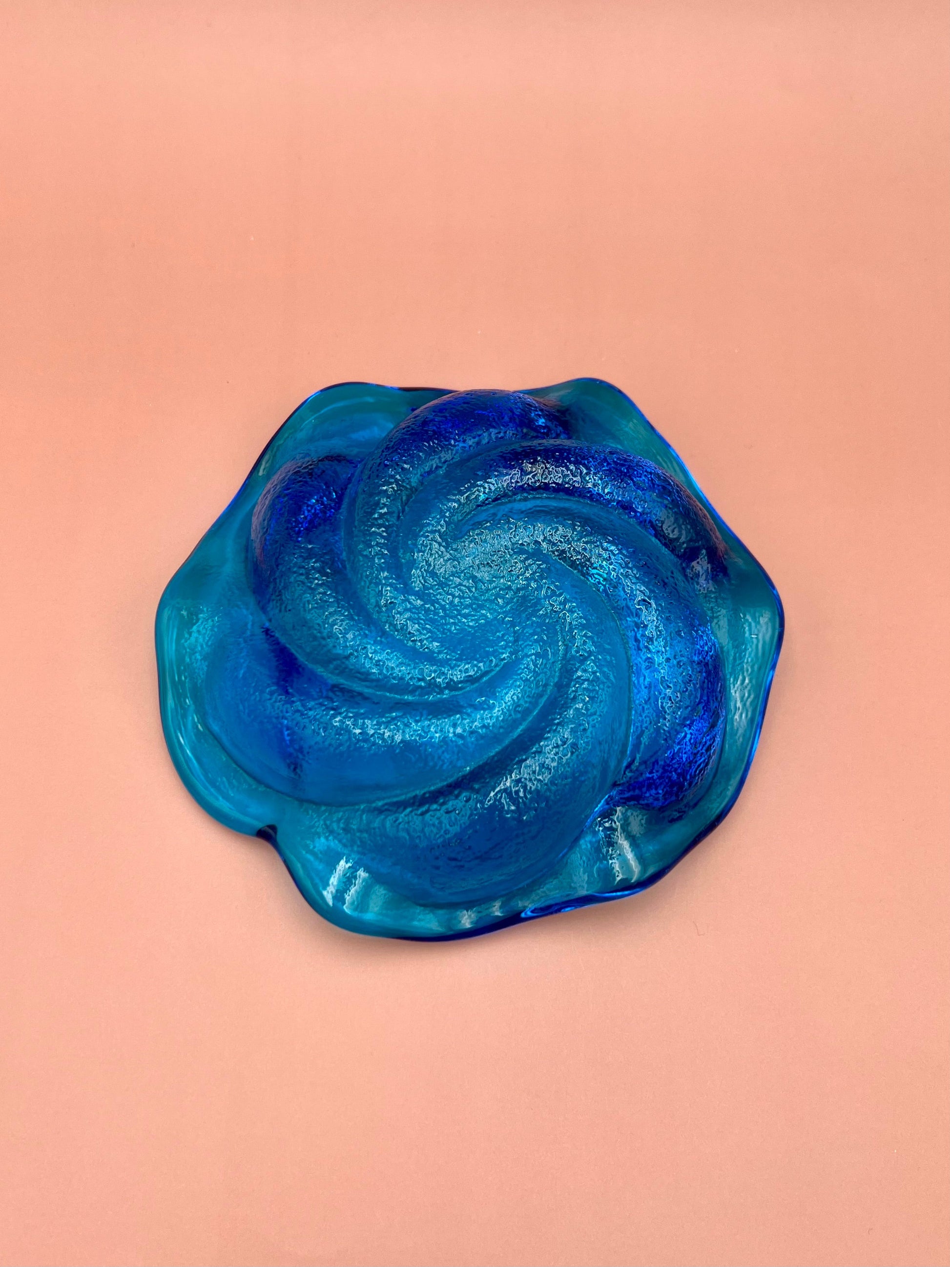 Blue and aqua swirled glass ashtray shown from a top-down angle, peach background