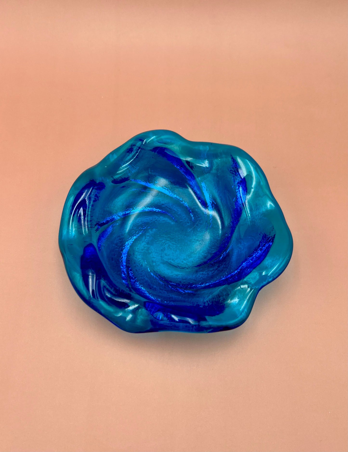 Blue and aqua swirled glass ashtray with a ruffled scalloped edge, peach background