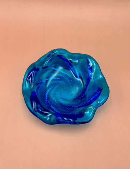 Blue and aqua swirled glass ashtray with a ruffled scalloped edge, peach background