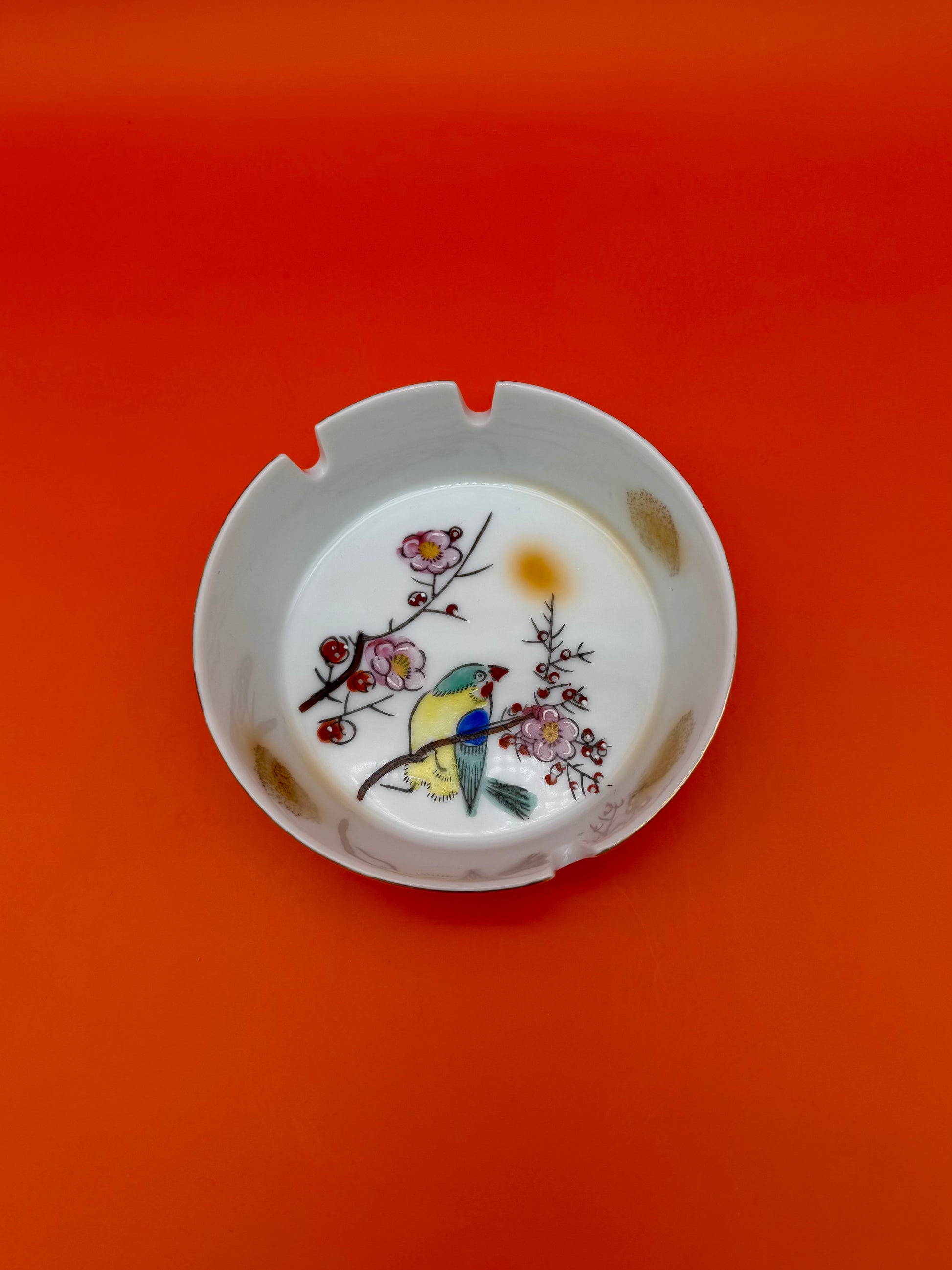 Same round cherry blossom and bird ashtray from the Verna Set shown from farther away, orange background.