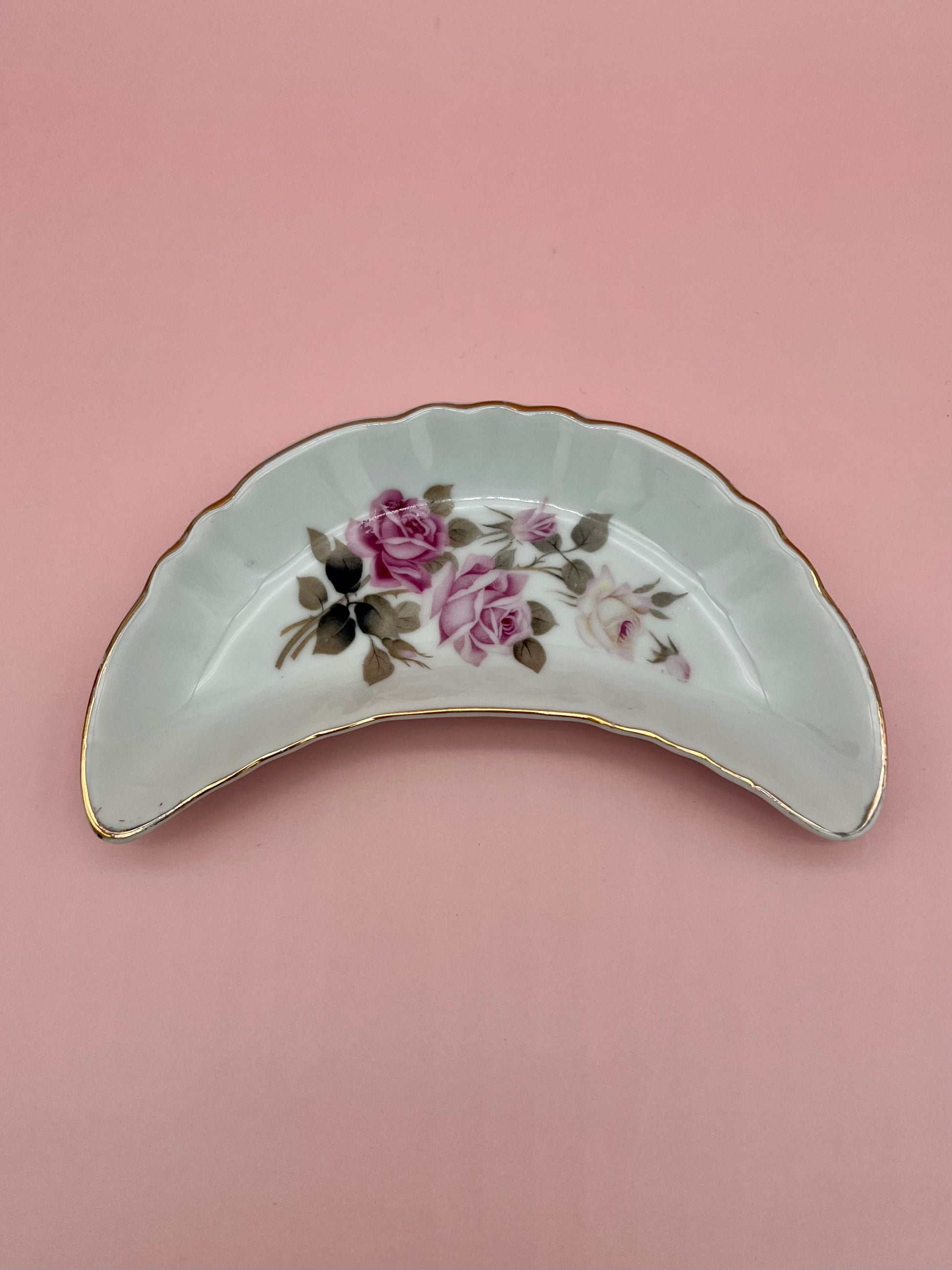 Crescent-shaped white porcelain ashtray with a teal and orange floral spray and gold trim, red-orange background