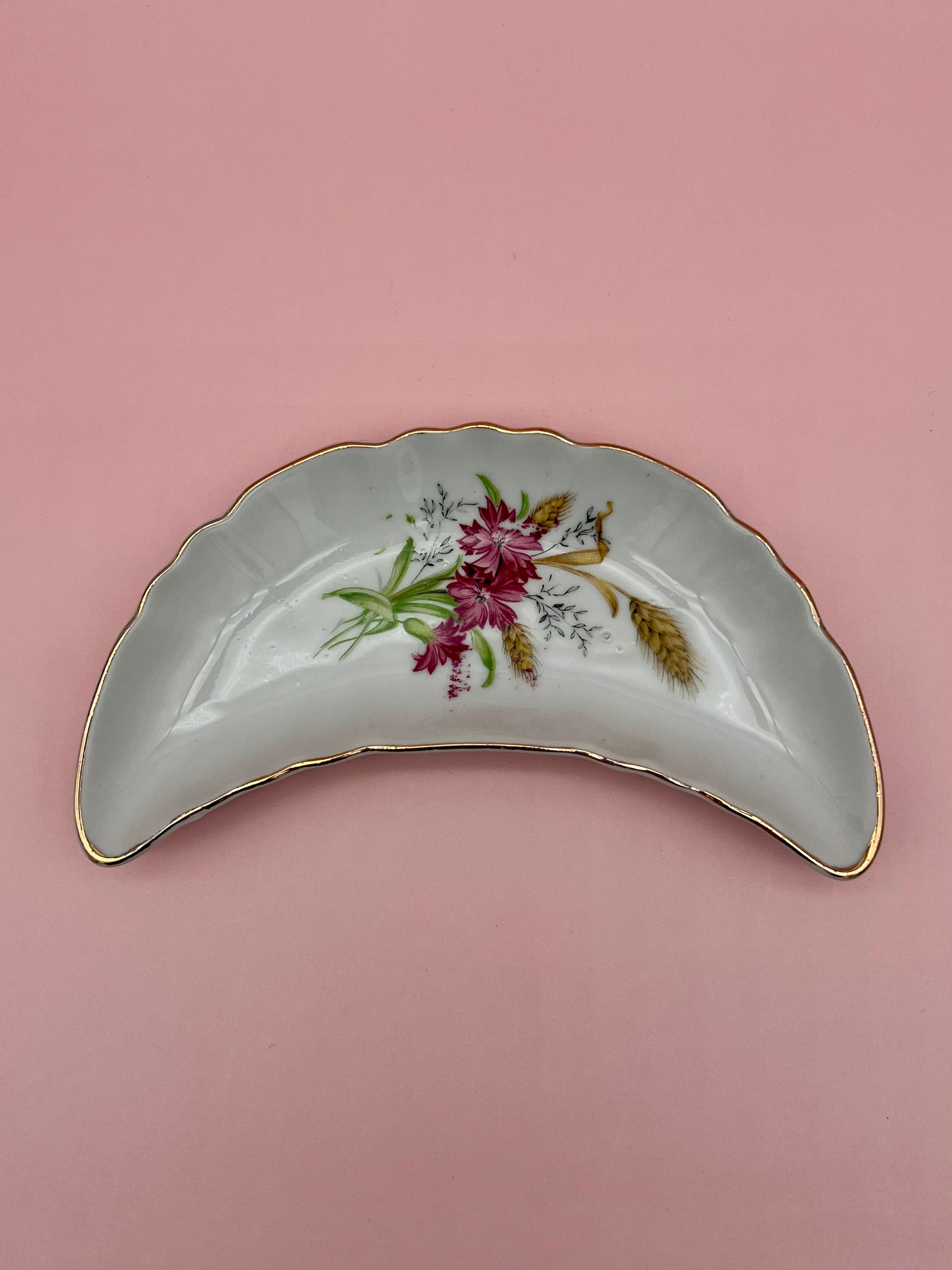 Crescent-shaped white porcelain ashtray with a red and pink rose floral spray and gold trim, pink background