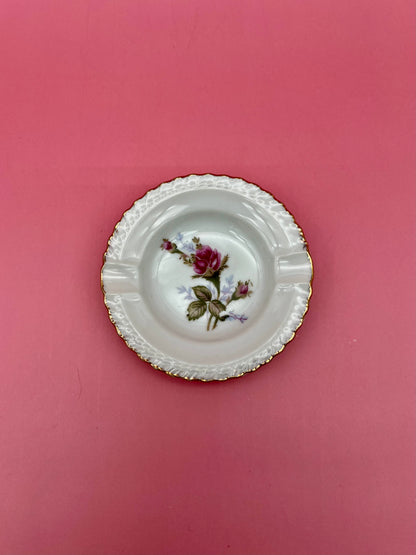 Round scalloped white ashtray with an embossed rim, hand-painted with a single pink rose, pink background.