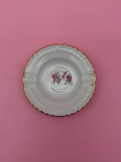 Round scalloped white ashtray with a deep ridged rim, hand-painted with a small pink rose bouquet in the center, pink background.