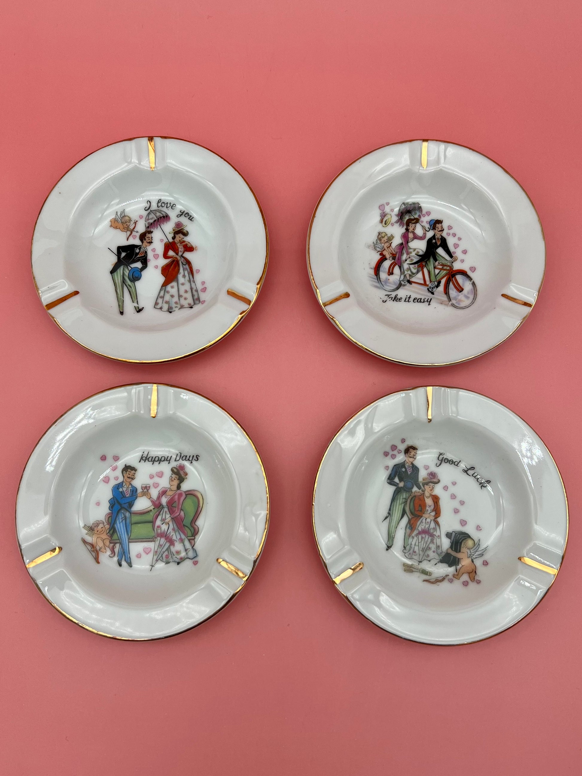 Set of four small round white ceramic ashtrays, each hand-painted with a different vintage romantic couple illustration and gold trim, coral background.